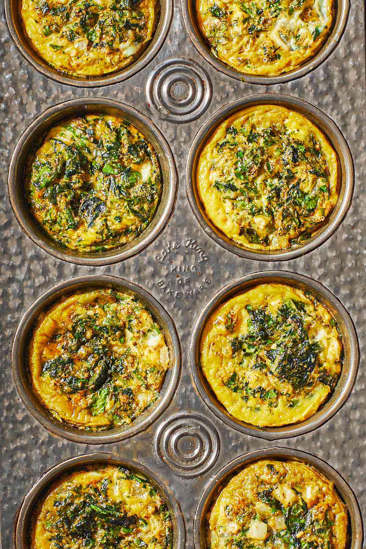 Overhead shot of Spanakopita egg muffins in a muffin tin, showing the herbs and spinach and golden edges.