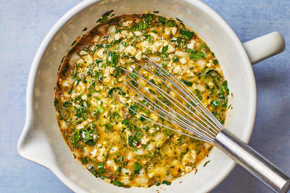 Spanakopita egg muffin batter being whisked in a bowl.