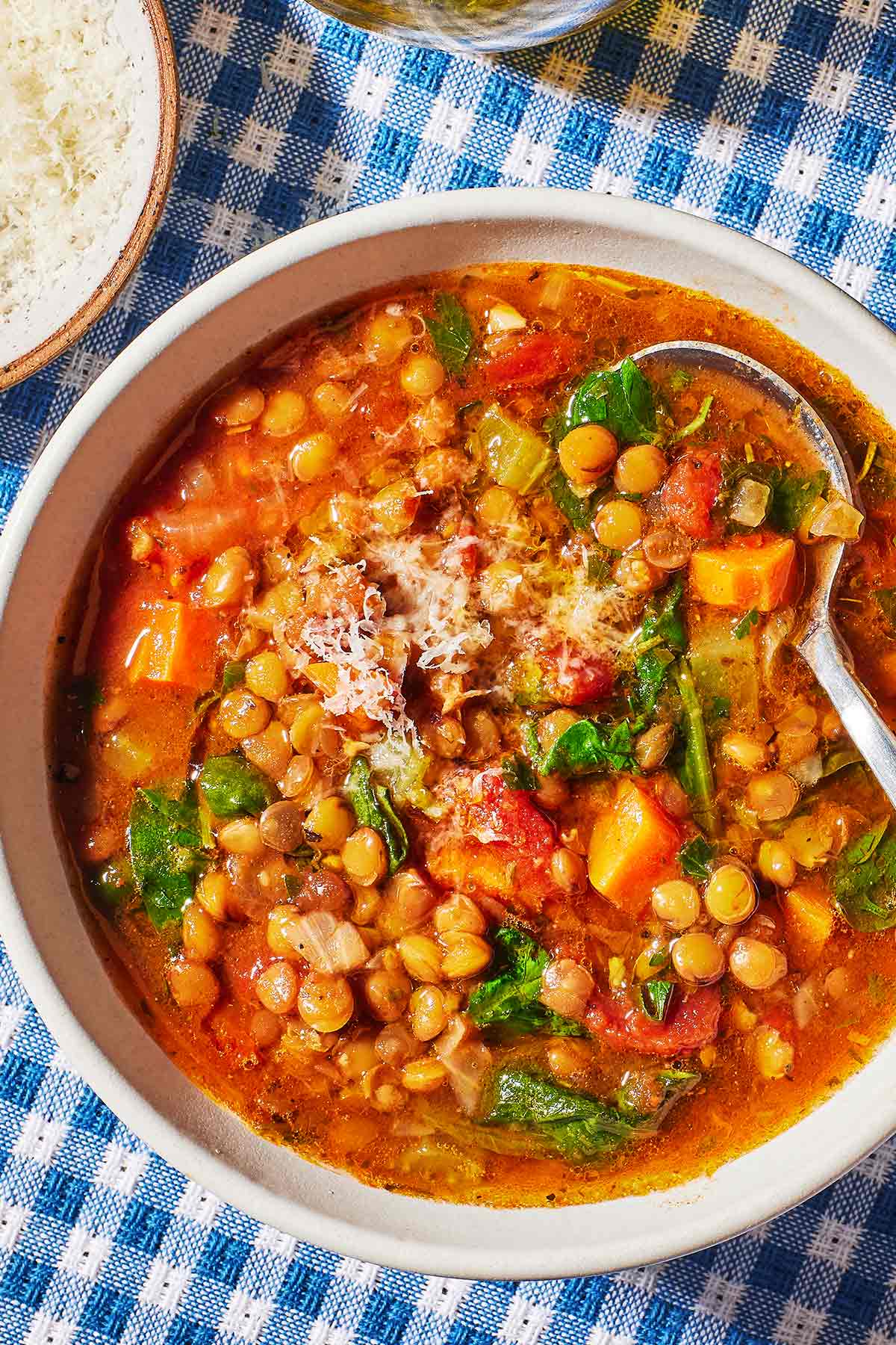 an overhead photo of italian lentil soup in a bowl with a spoon next to a small bowl of grated parmesan.