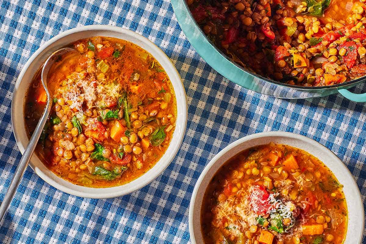 Two bowls of of Italian lentil soup, one with a spoon, next to a pot of the soup.