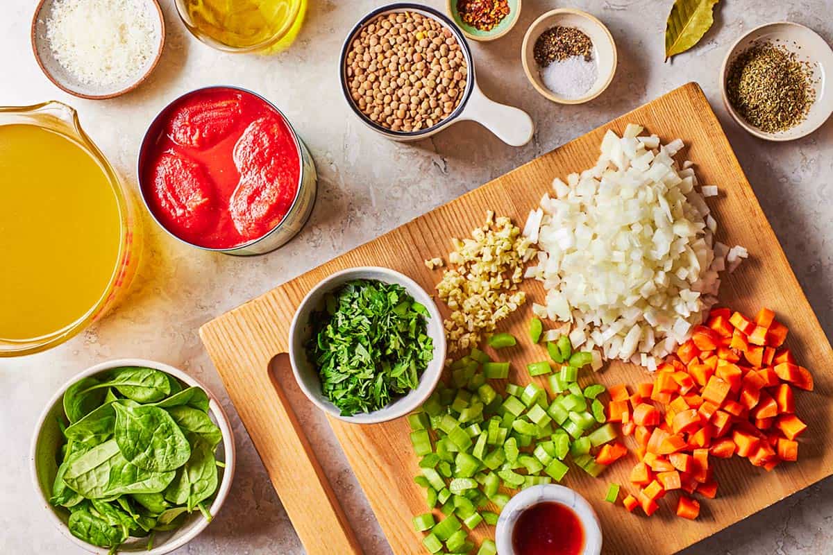 Ingredients for Italian lentil soup including olive oil, onion, garlic, carrots, celery, salt, pepper, canned whole tomatoes, vegetable broth, a bay leaf, Italian seasoning, red pepper flakes, lentils, baby spinach parsley, red wine vinegar, and grated parmesan cheese.
