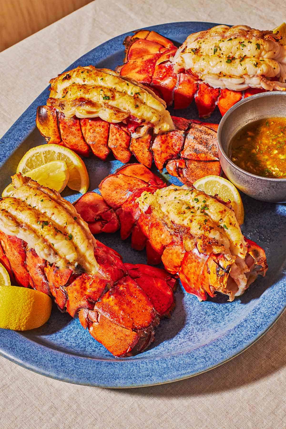 4 broiled lobster tails on a blue serving platter lemon wedges and butter sauce in a small bowl.