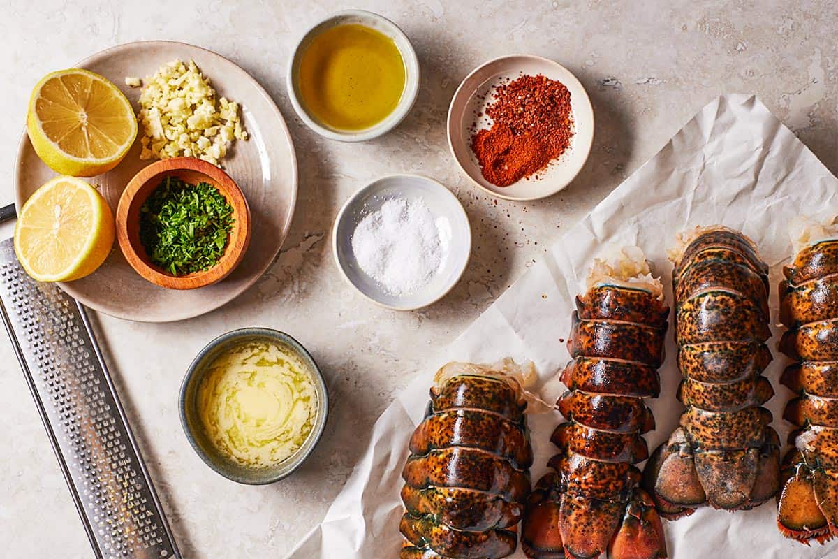 Ingredients for broiled lobster tail including 4 lobster tails, olive oil, butter, garlic, lemon, chopped parsley, sweet paprika, Aleppo and Kosher salt.