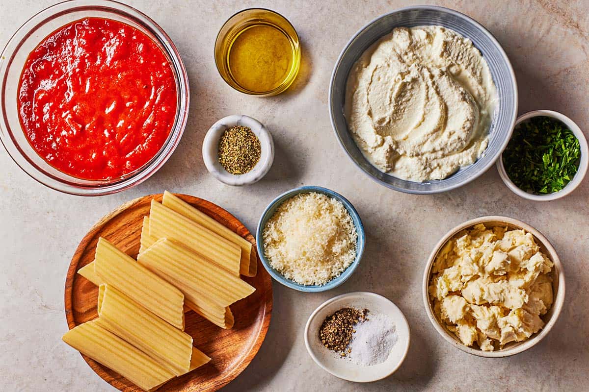 Ingredients for Manicotti including uncooked manicotti, ricotta cheese, mozzarella, grated parmesan, parsley, Italian seasoning, black pepper, olive oil and spaghetti sauce.