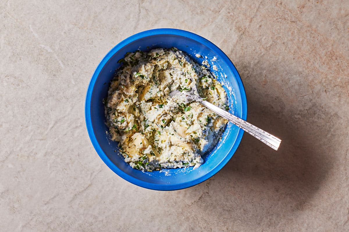 Filling for the manicotti in a blue bowl with a spoon.