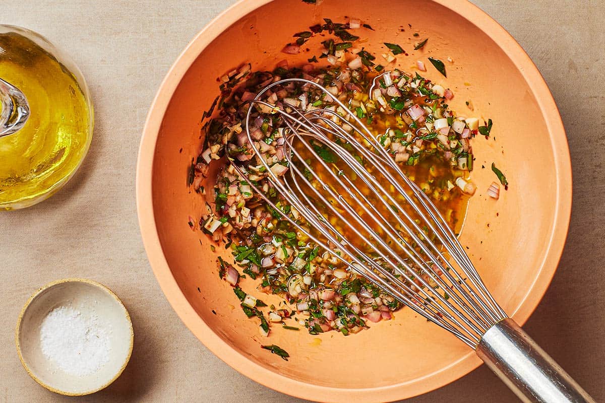 marinade for the mushrooms being mixed in a bowl with a whisk next to a small pitcher of olive oil and small bowl of kosher salt.