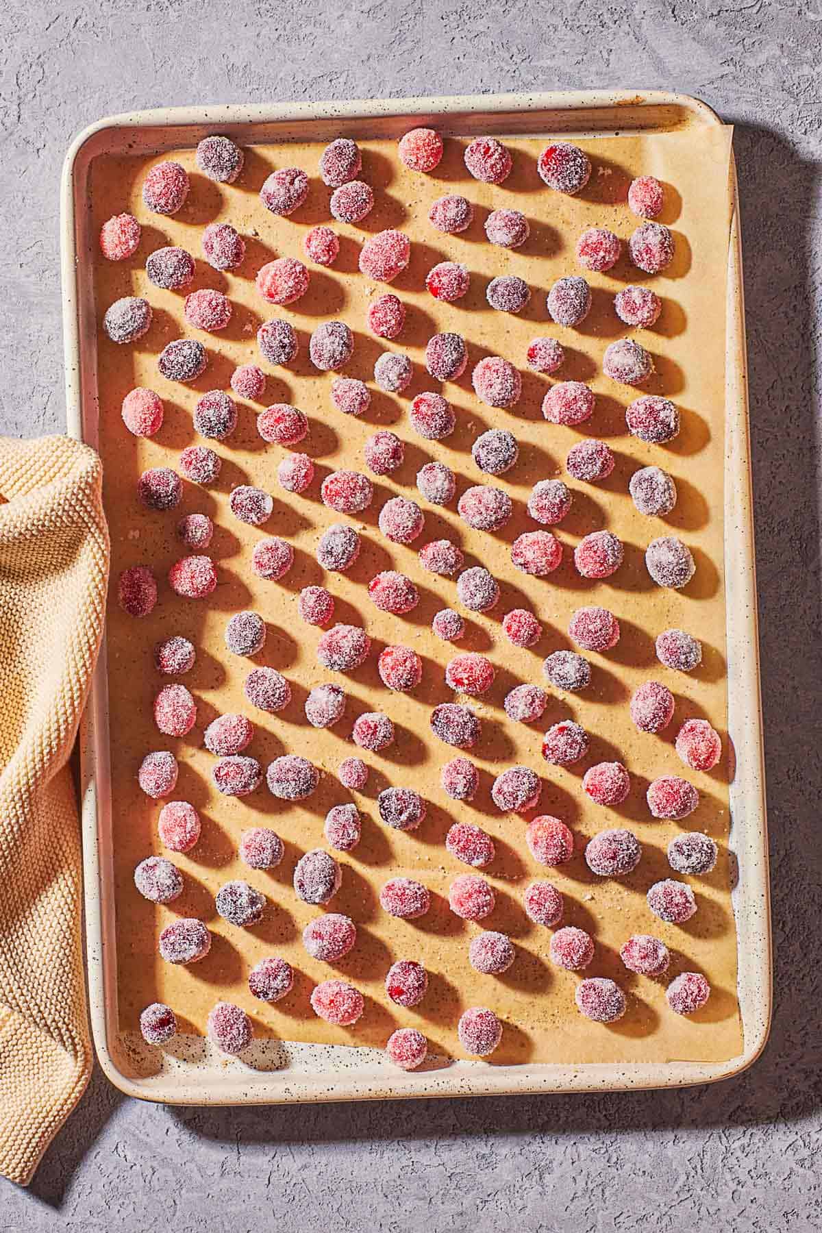 sugared cranberries spread evenly on a baking sheet lined with parchment paper.