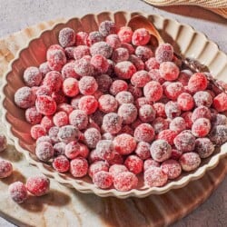 sugared cranberries in a serving bowl with a spoon next to a cloth napkin.