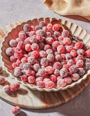 sugared cranberries in a serving bowl with a spoon next to a cloth napkin.