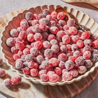 sugared cranberries in a serving bowl with a spoon next to a cloth napkin.