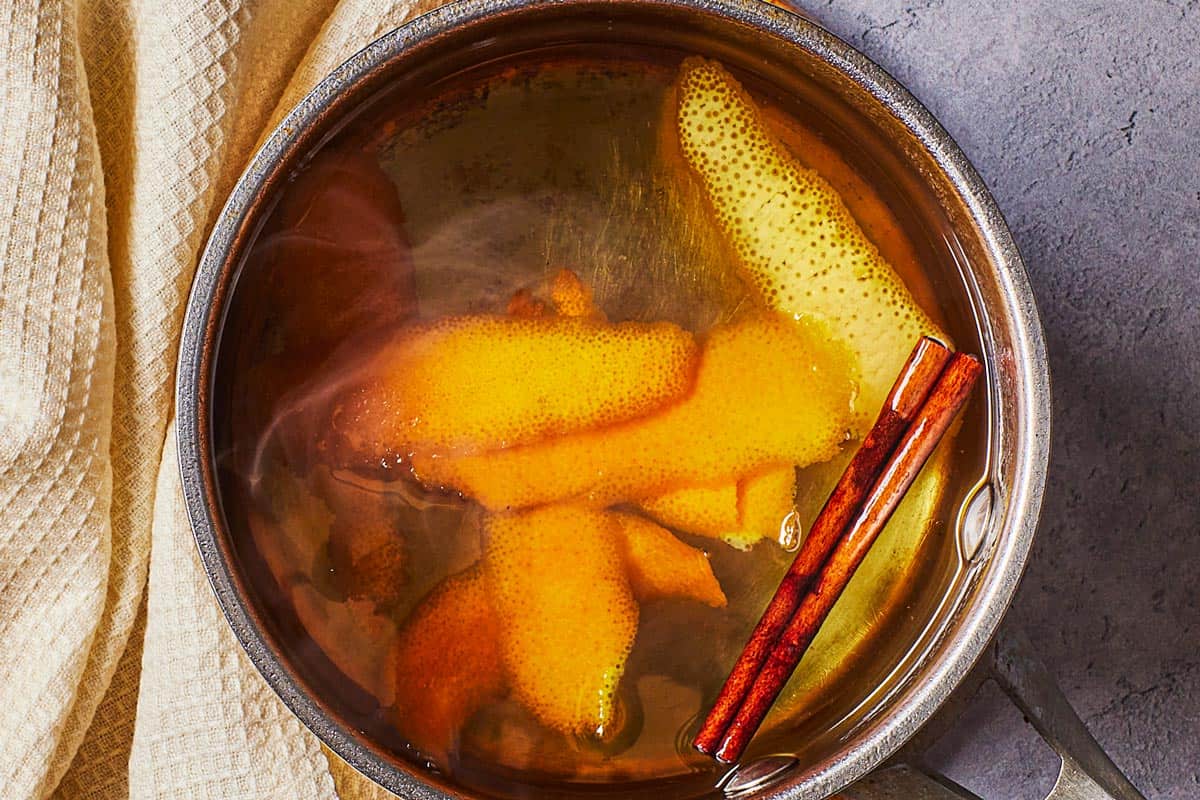 an overhead photo of the orange peel and cinnamon stick after being added to the simmering simple syrup in a saucepan.