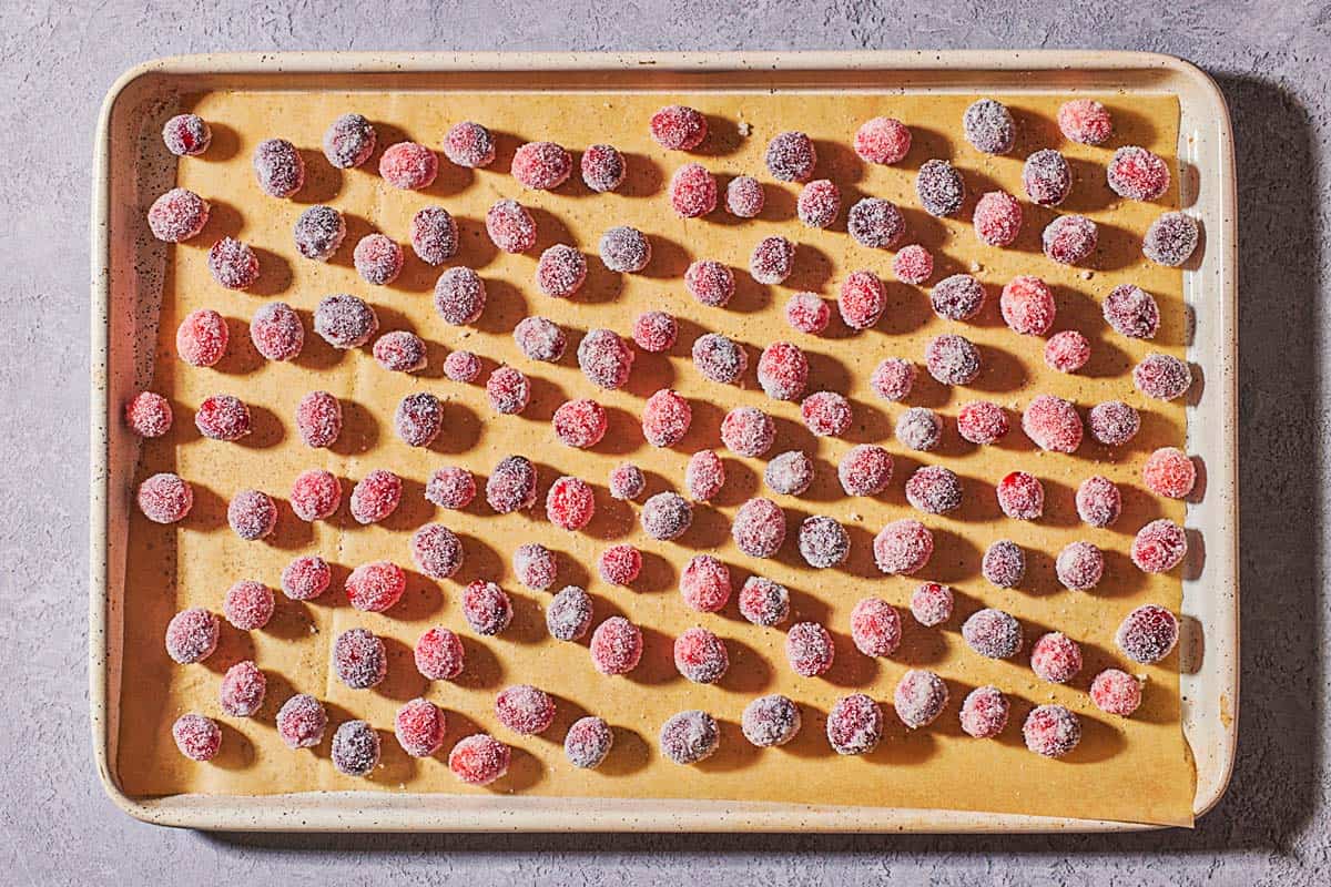 sugared cranberries spread evenly on a baking sheet lined with parchment paper.