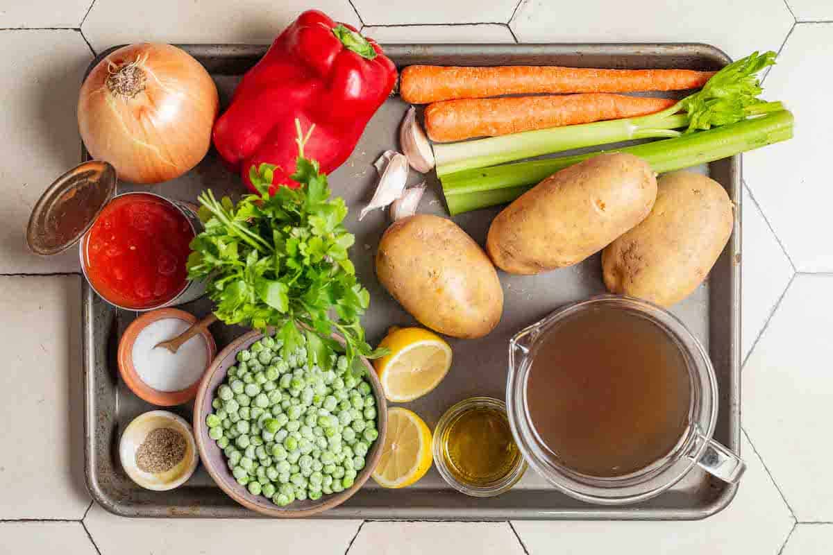 ingredients for vegetable stew including olive oil, onion, garlic, celery, carrots, potatoes, red bell pepper, salt, pepper, frozen peas, diced tomatoes, vegetable broth, parsley, and lemon.