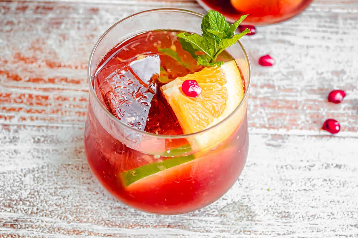 a close up of a glass of holiday punch garnished with orange and lime slices and mint.