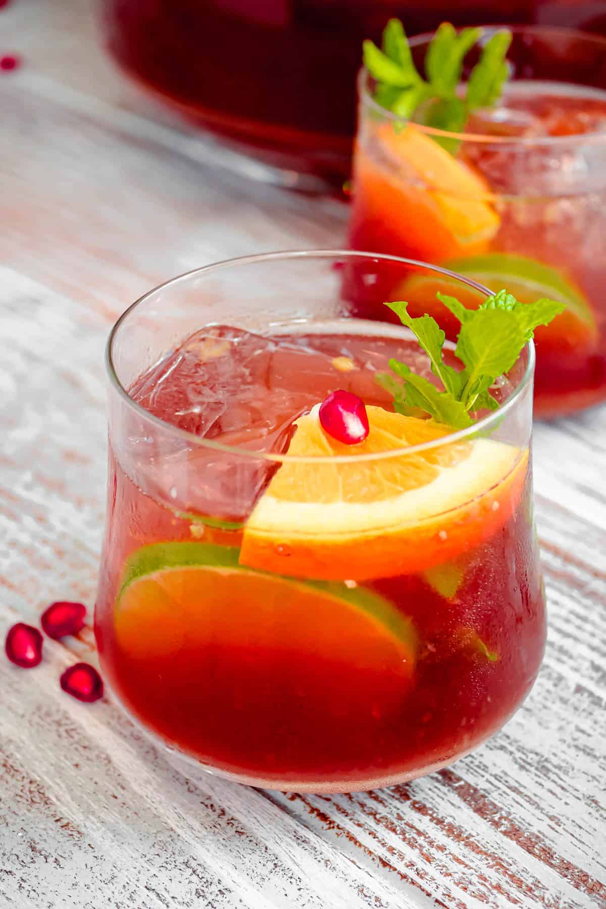two glasses of holiday punch garnished with orange and lime slices and mint.