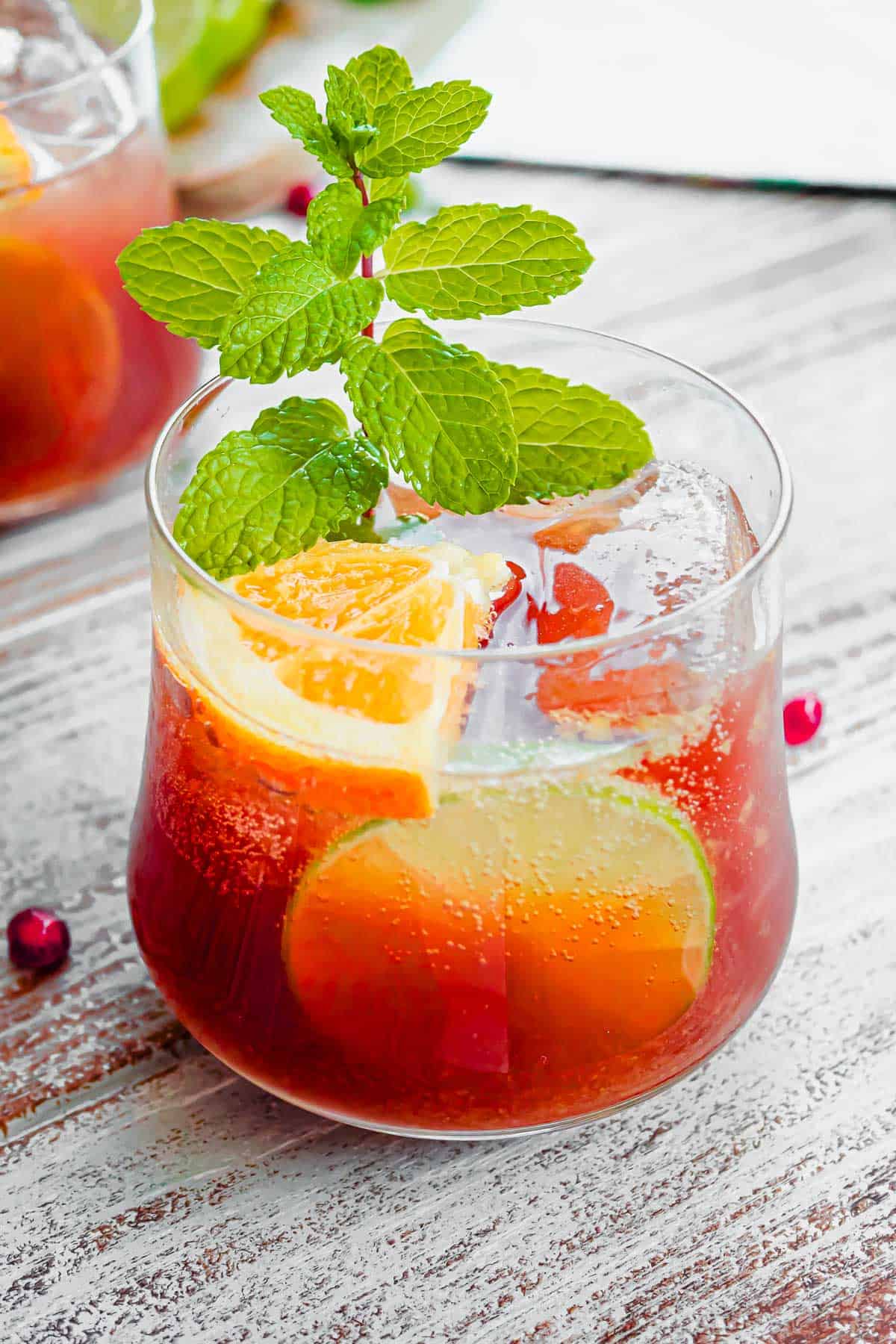 a close up of a glass of holiday punch garnished with orange and lime slices and mint.
