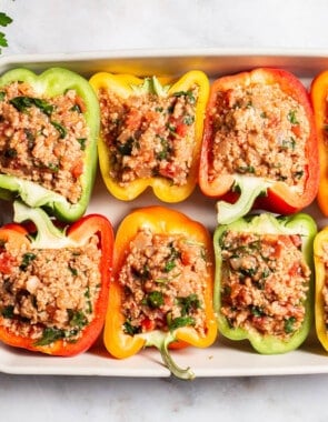 An overhead photo of 8 uncooked chicken stuffed peppers in a baking dish next to a bunch of parsley.