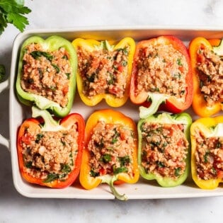 An overhead photo of 8 uncooked chicken stuffed peppers in a baking dish next to a bunch of parsley.