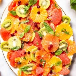an overhead photo of citrus salad on a serving platter surrounded basil and a small bowl of pomegranate seeds.