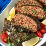 A close up of the greek meatloaf sliced on a serving platter with garnishes of cherry tomatoes, lemon wedges and parsley.