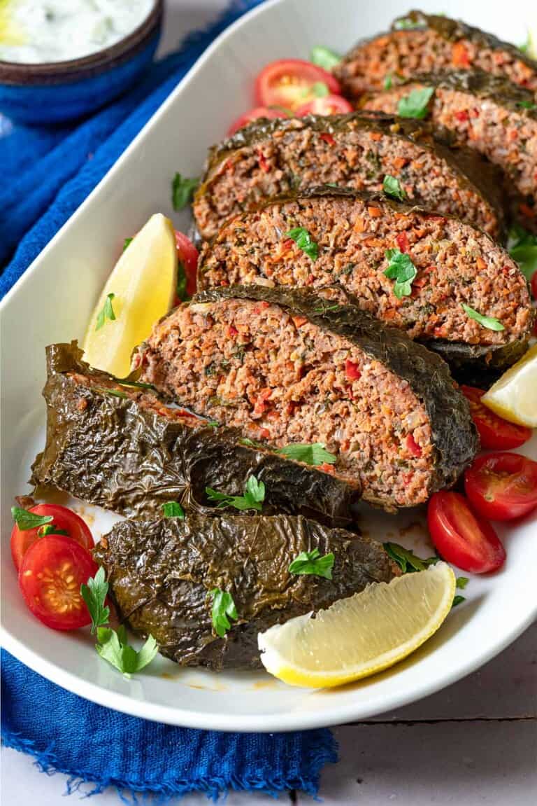 A close up of the greek meatloaf sliced on a serving platter with garnishes of cherry tomatoes, lemon wedges and parsley.