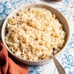 Brown rice in a bowl with a spoon next to a small bowl of salt with a spoon and a cloth napkin.