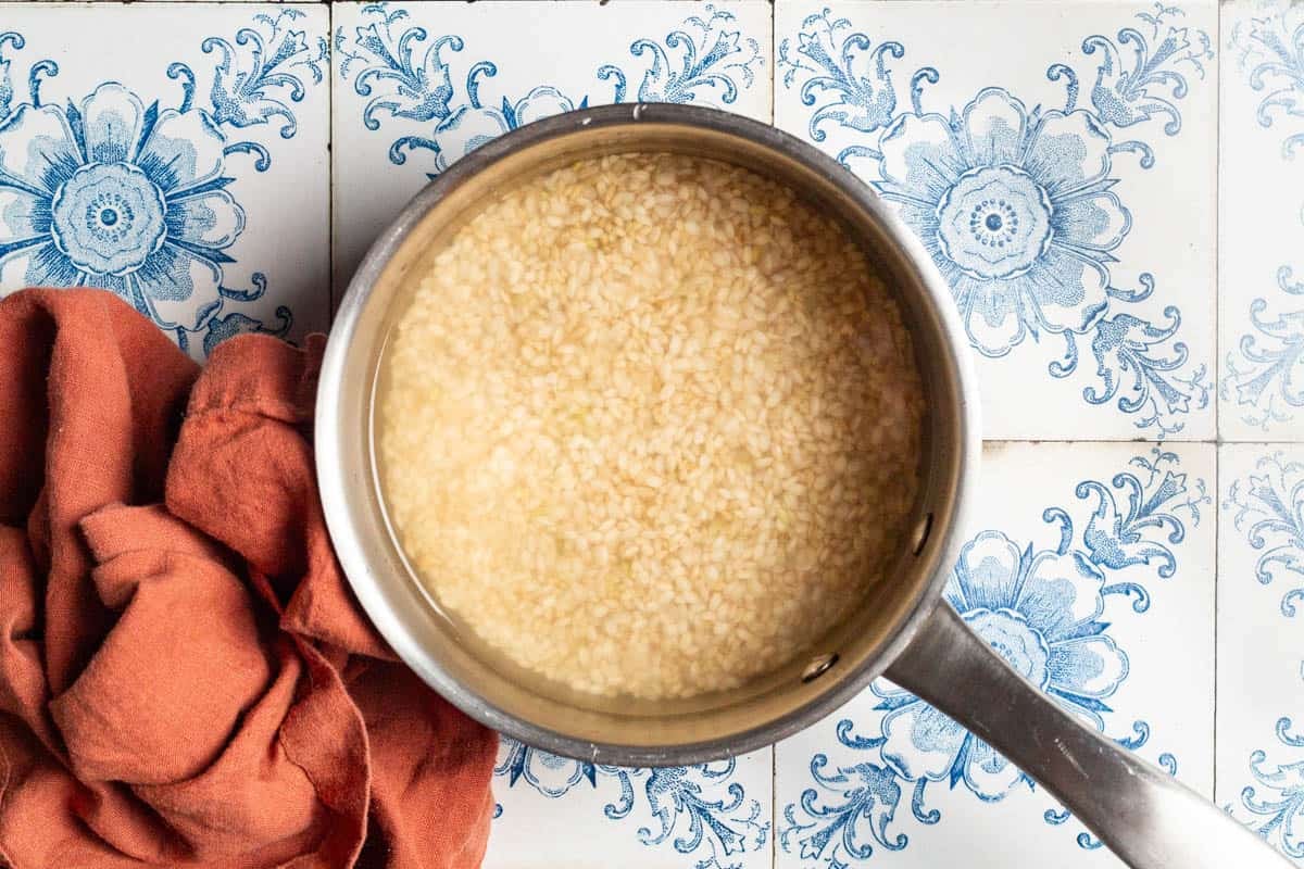 An overhead photo of brown rice soaking in a saucepan next to a cloth napkin.