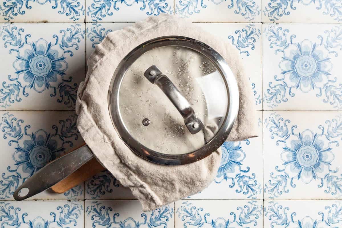 The saucepan of brown rice covered with a clean kitchen towel and a lid.