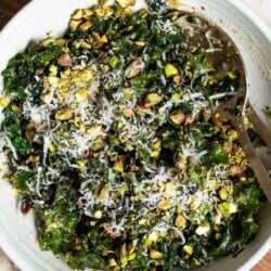 An overhead photo of kale salad in a large bowl with serving utensils on a cutting board.