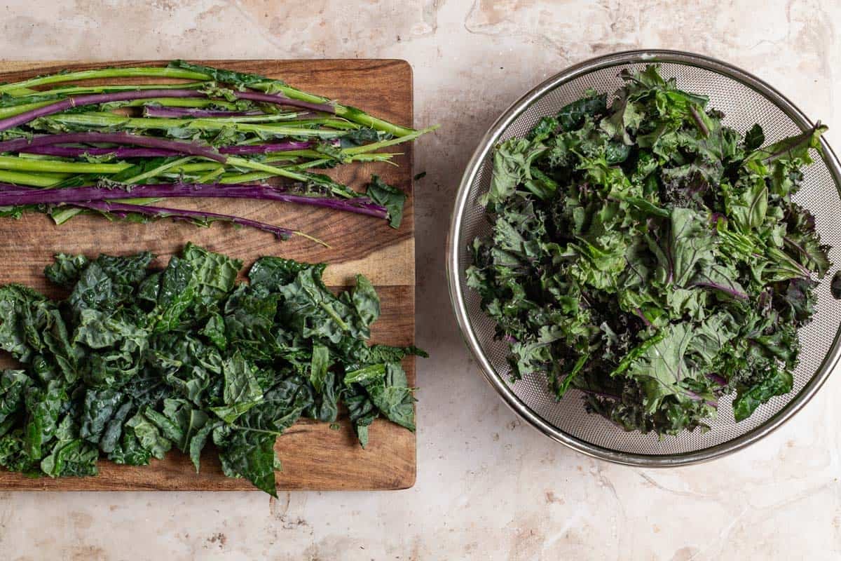 Chopped kale on a cutting board next to the stems. Next to this is a colander with more chopped kale.