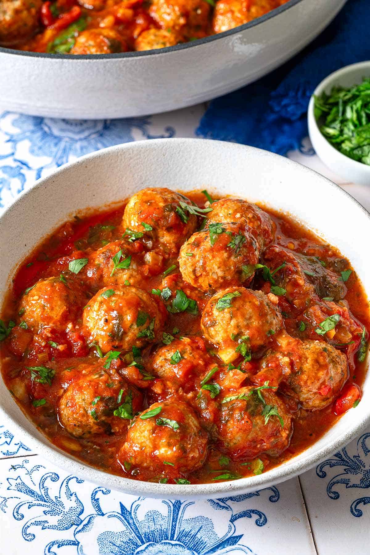 a serving of moroccan fish kofta in a bowl next to the pot of the kofta and a small bowl of parsley.