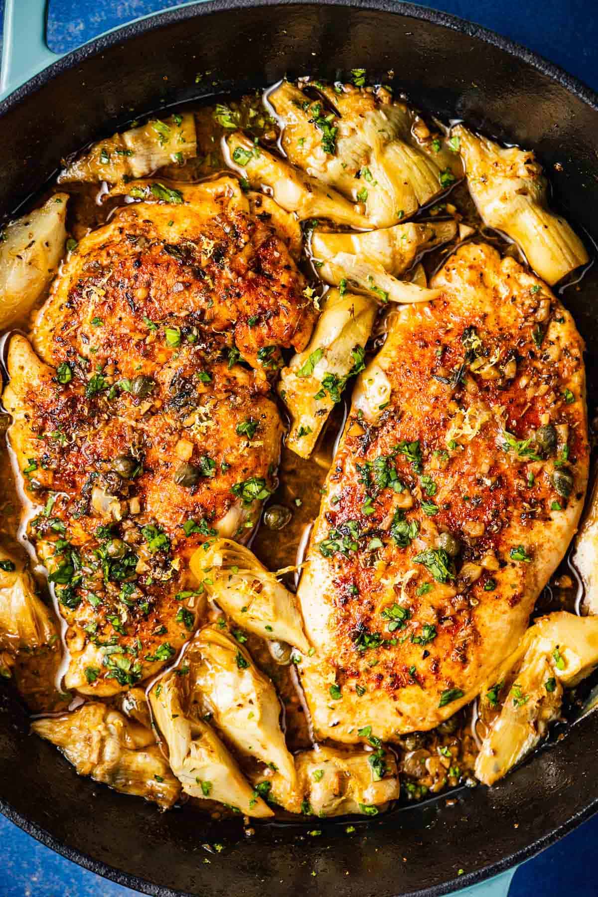 overhead photo of cooked artichoke chicken in a cast iron skillet.