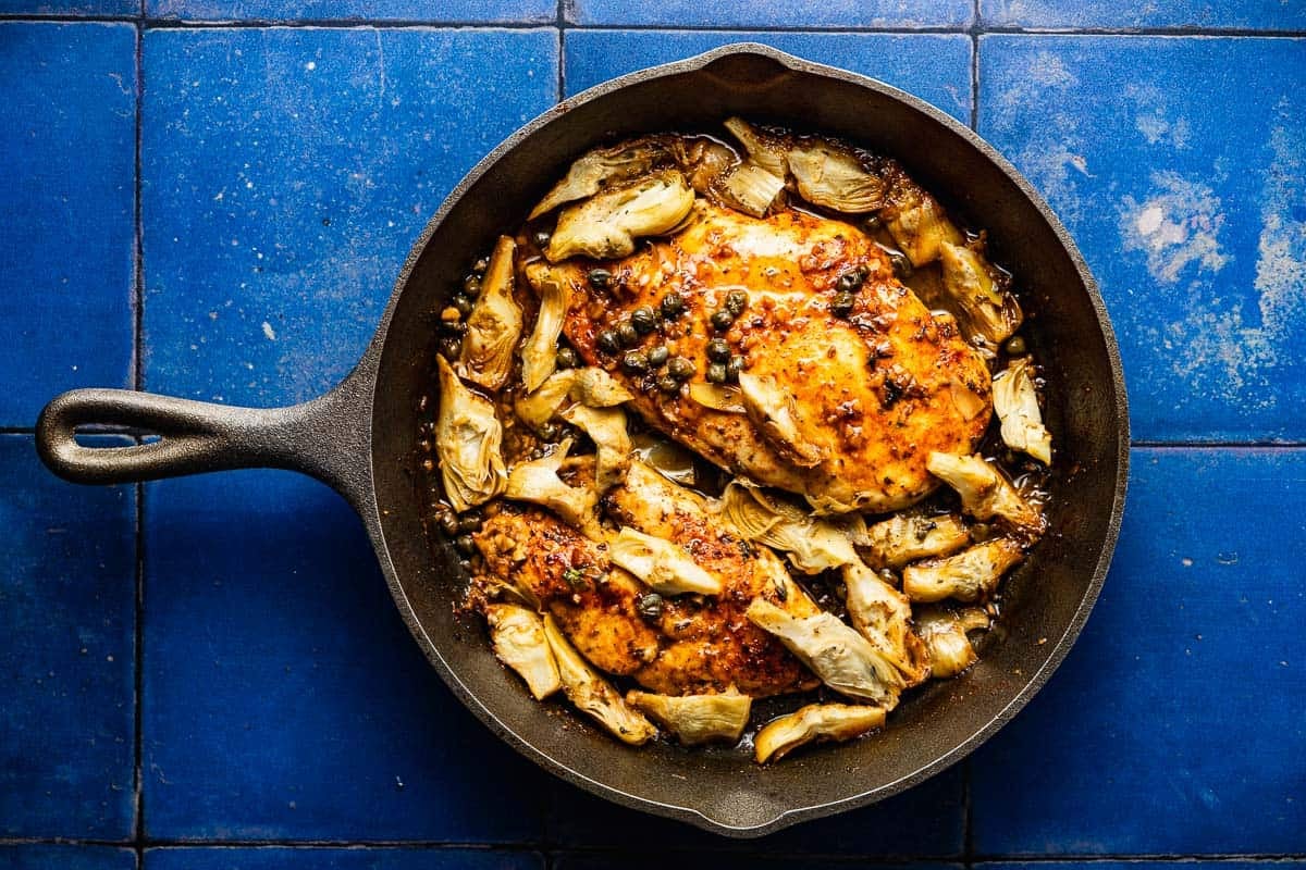 an overhead photo of cooked artichoke chicken in a cast iron skillet.