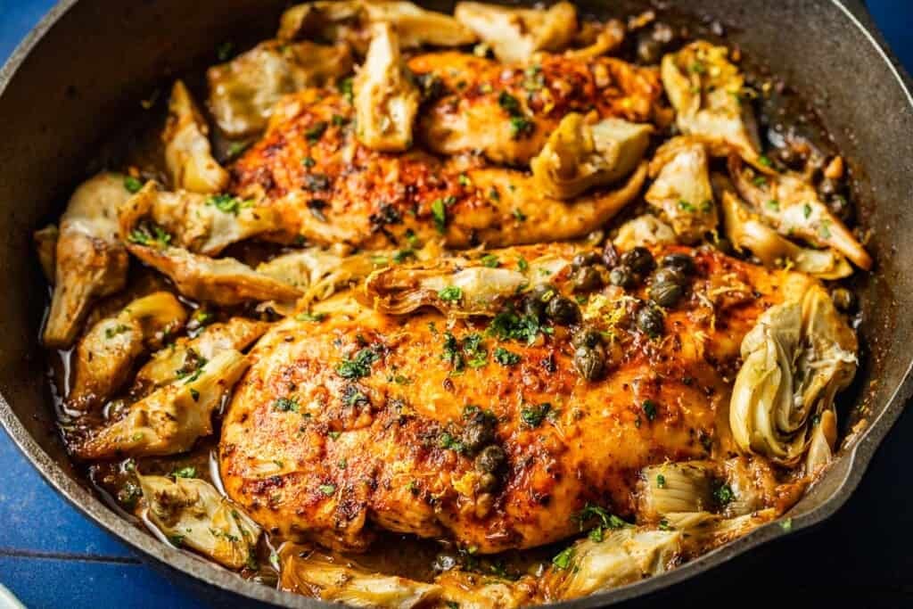 a close up of cooked artichoke chicken in a cast iron skillet.