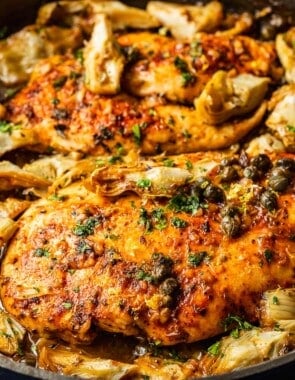 a close up of cooked artichoke chicken in a cast iron skillet.