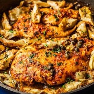 a close up of cooked artichoke chicken in a cast iron skillet.