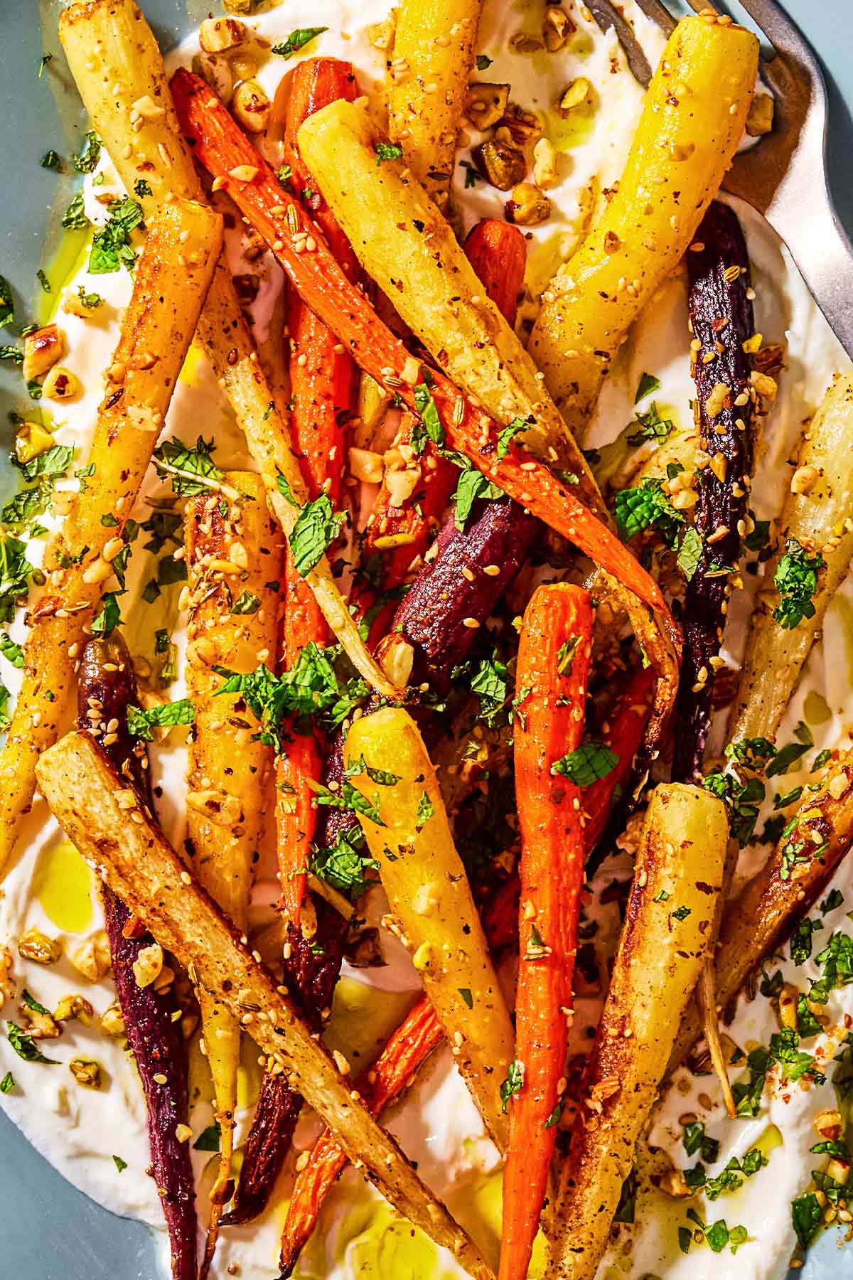 A close up photo of roasted rainbow carrots with with dukkah, mint and a garlicky yogurt sauce on a serving platter.