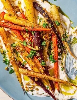 An overhead close up of roasted rainbow carrots with with dukkah, mint and a garlicky yogurt sauce on a serving platter with a fork.