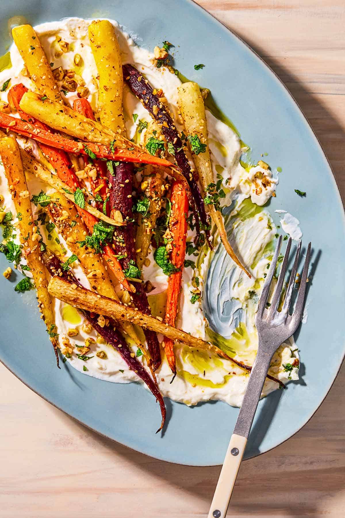 An overhead photo of roasted rainbow carrots with with dukkah, mint and a garlicky yogurt sauce on a serving platter with a fork.