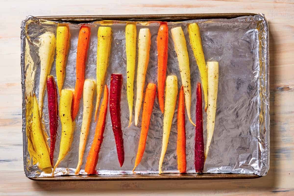 rainbow carrots seasoned with salt and pepper on a foil-lined baking sheet.