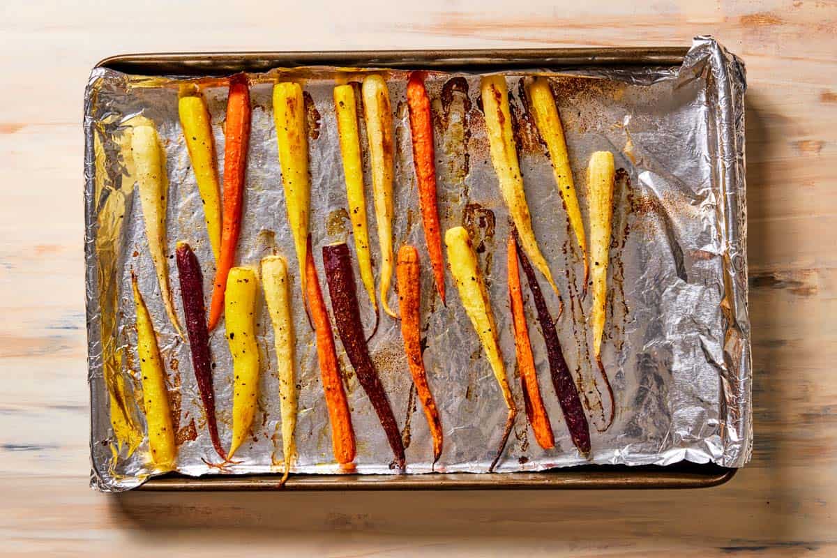 baked rainbow carrots seasoned with salt and pepper on a foil-lined baking sheet.