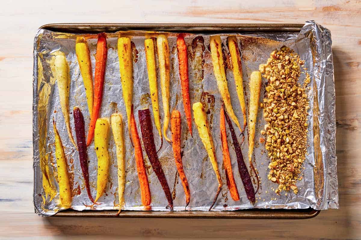 baked rainbow carrots seasoned with salt and pepper and bit of dukkeh on the side on a foil-lined baking sheet.