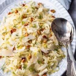 Side shot of fennel salad with two silver serving spoons.