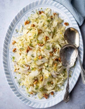 Overhead shot of fennel salad on a blue and white serving platter with two silver serving spoons.