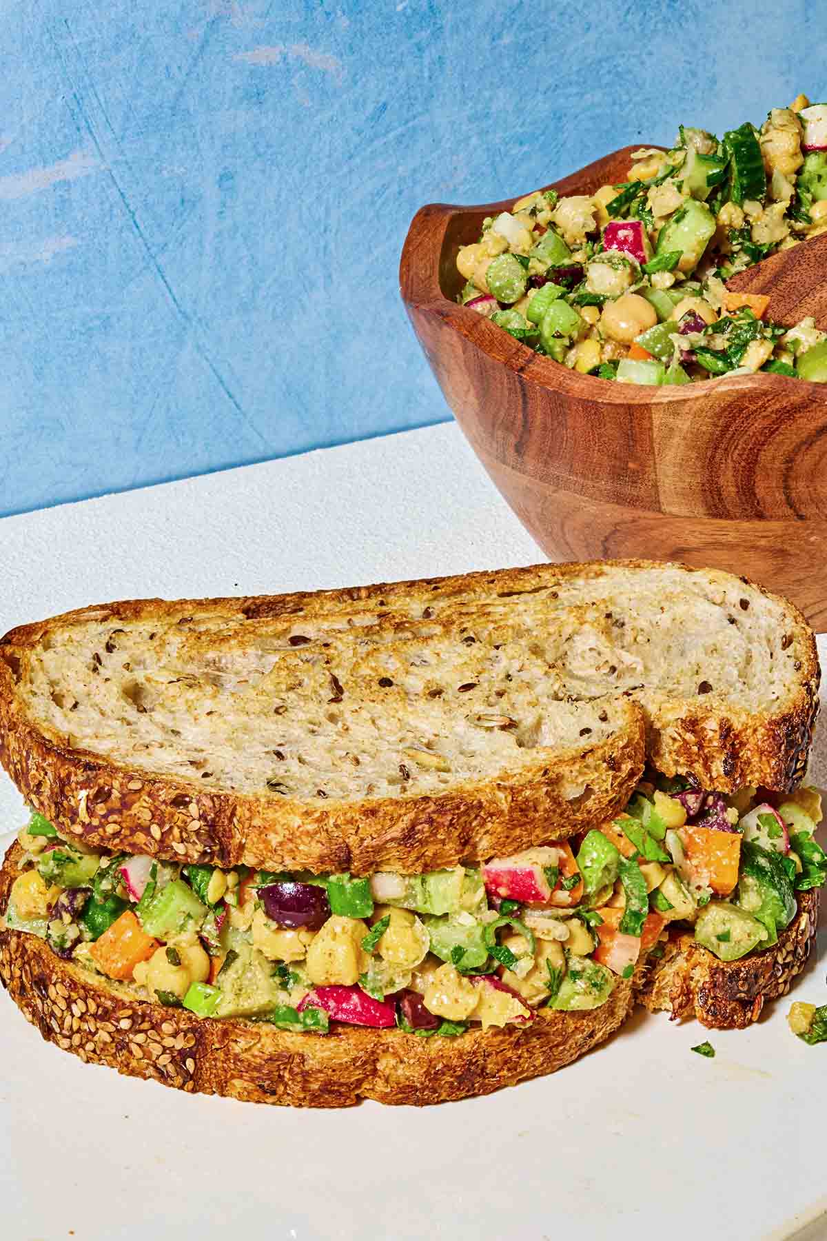 A close up of a vegan chickpea salad sandwich in front of a bowl of chickpea salad.