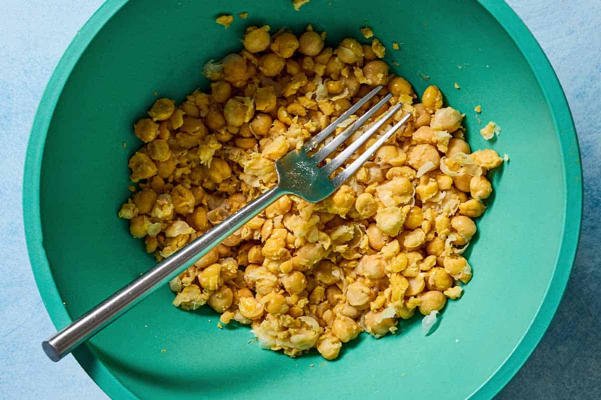 Chickpeas in a mixing bowl just after being slightly smashed with a fork.