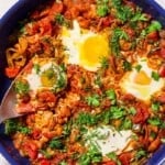 An overhead photo of white bean shakshuka garnished with dill and parsley in a skillet with a serving spoon.