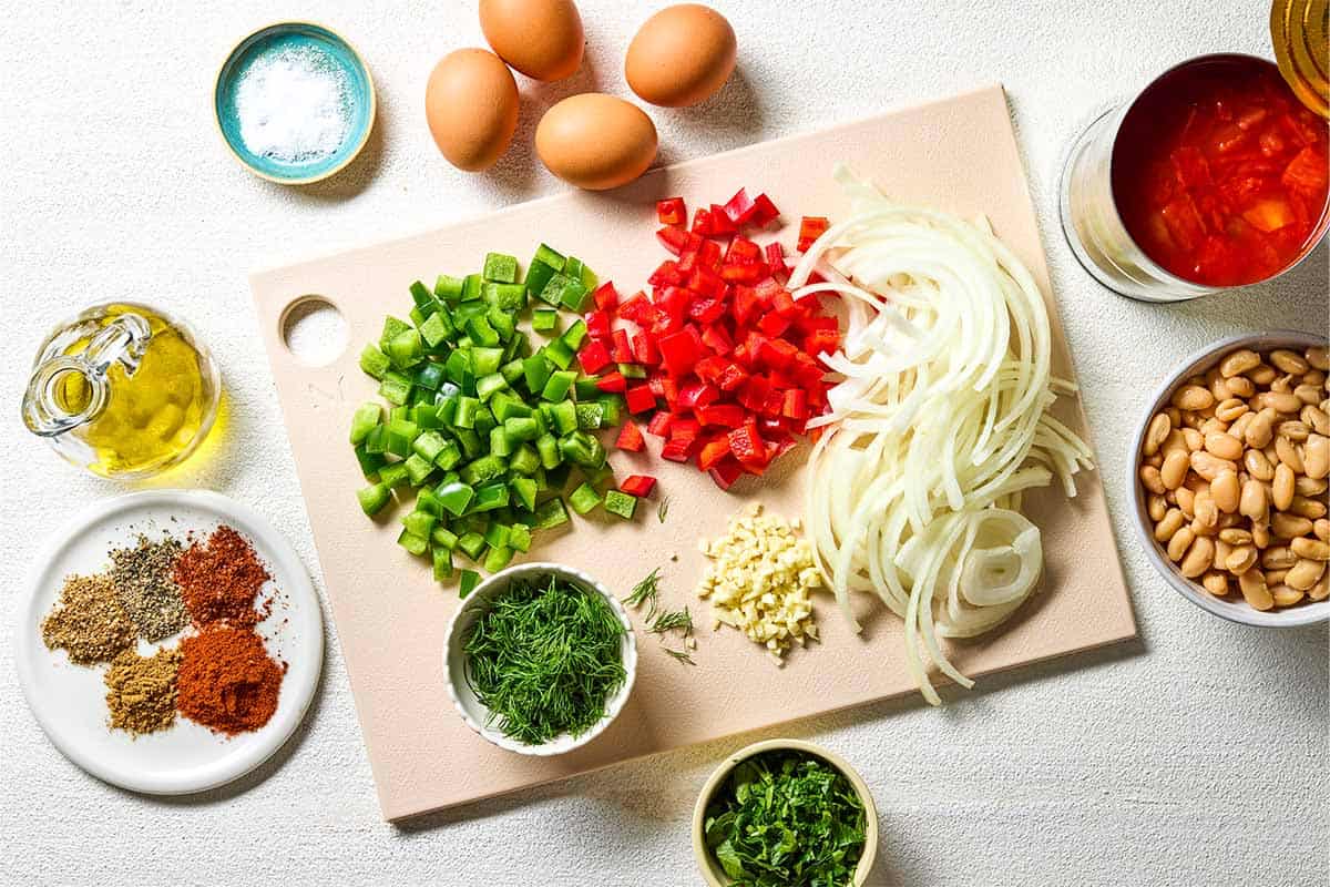 ingredients for white bean shakshuka including eggs, canned diced tomatoes, cannellini beans, olive oil, onion, green pepper, red pepper, garlic, coriander, paprika, cumin, aleppo pepper, salt, black pepper, parsley and dill.