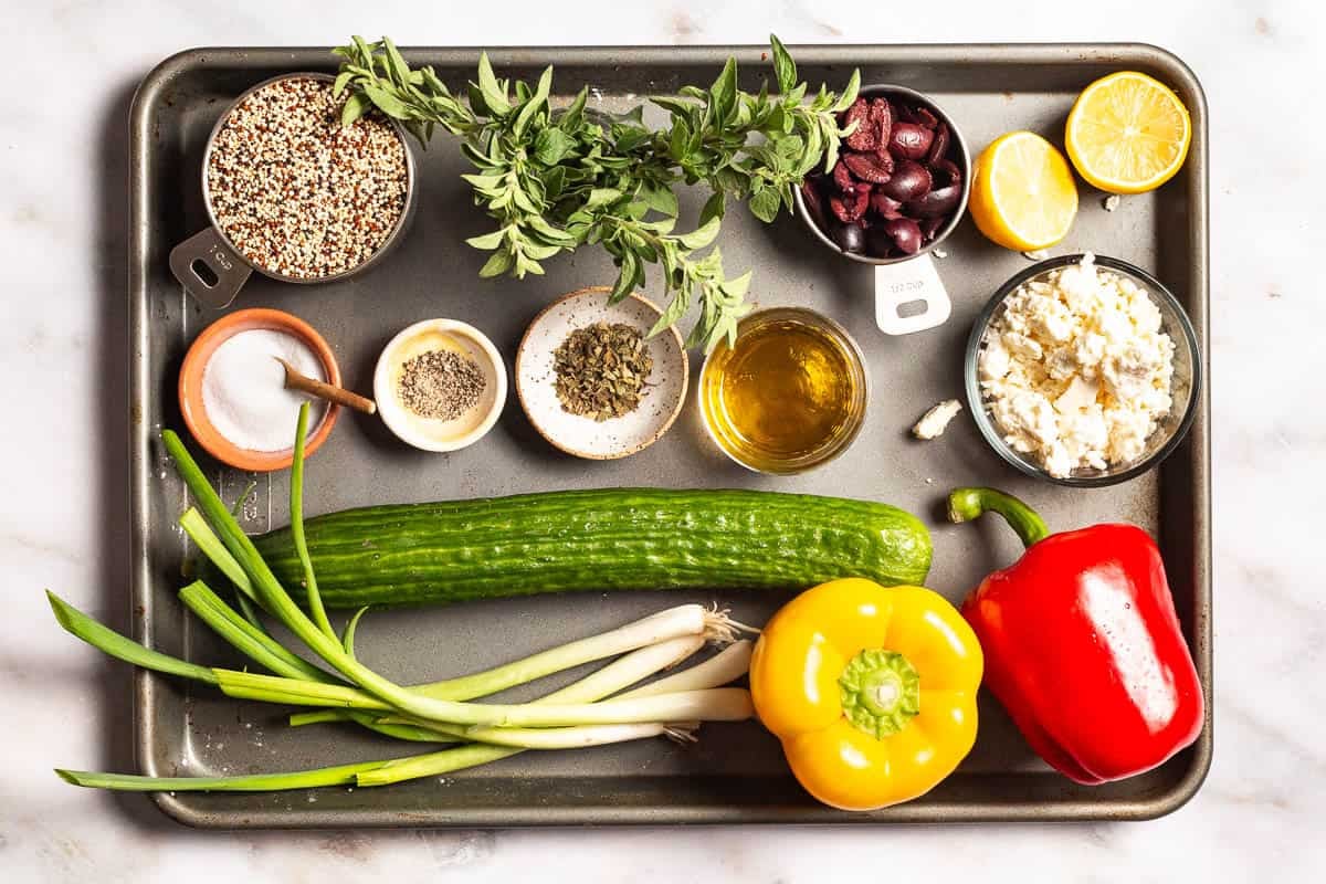 ingredients for quinoa salad including quinoa, lemon, oregano, salt, pepper, olive oil, scallions, bell peppers, kalamata olives, English cucumber, and crumbled feta cheese.