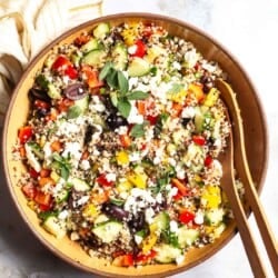 An overhead photo of quinoa salad in a large bowl with wooden serving utensils next to a cloth napkin.